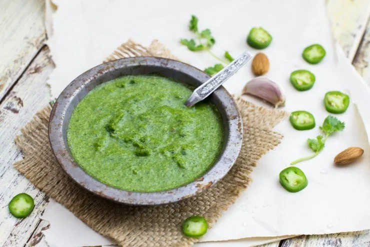 cilantro chutney in a small bowl on a burlap square with green chili slices around