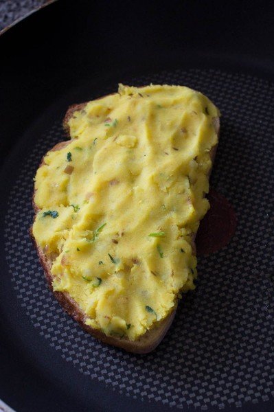 The bread and potato layer of the masala cheese toast sandwich cooking on a pan