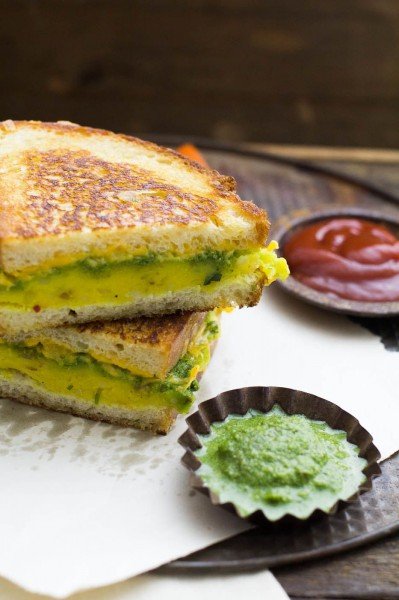 masala cheese toast sandwich halves layered on top of each other with ketchup and chutney on white paper