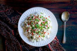 A white bowl of Cucumber Raita with a spoon on the side