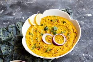 moong dal in a white flower shaped bowl garnished with raw red onion rings, lemon slices and cilantro