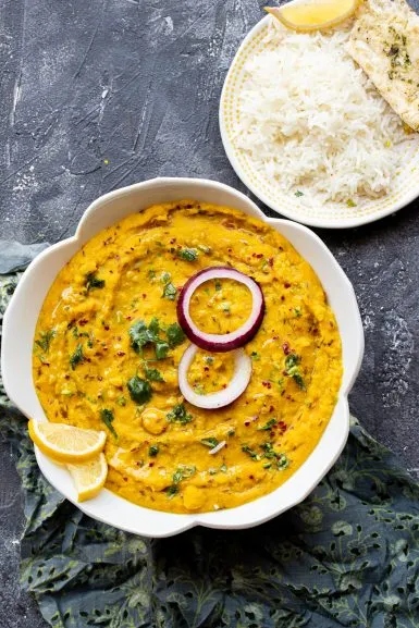 moong dal in a white bowl garnished with raw red onion and cilantro with a side of rice and naan