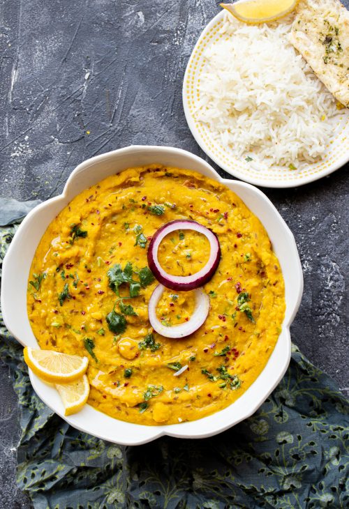 moong dal in a white bowl garnished with raw red onion and cilantro with a side of rice and naan