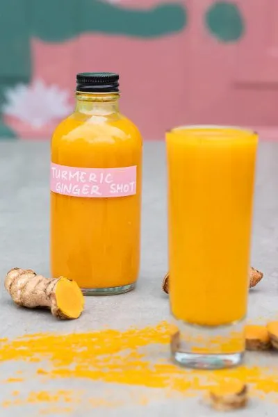 Ginger Turmeric Shots, a poured glass in front of the bottle with some turmeric nearby