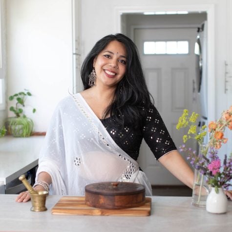 Puja standing in kitchen with masala dabba and mortar and pestle.