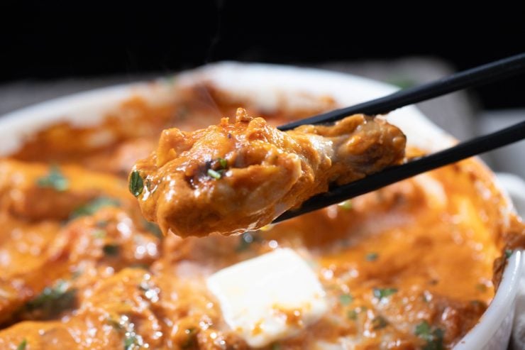Holding up a drummette of smothered butter chicken with tongs.